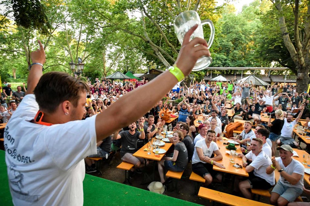 Feiernde Student mit leeren Bierglas in der Hand vor einen vollem Biergarten
