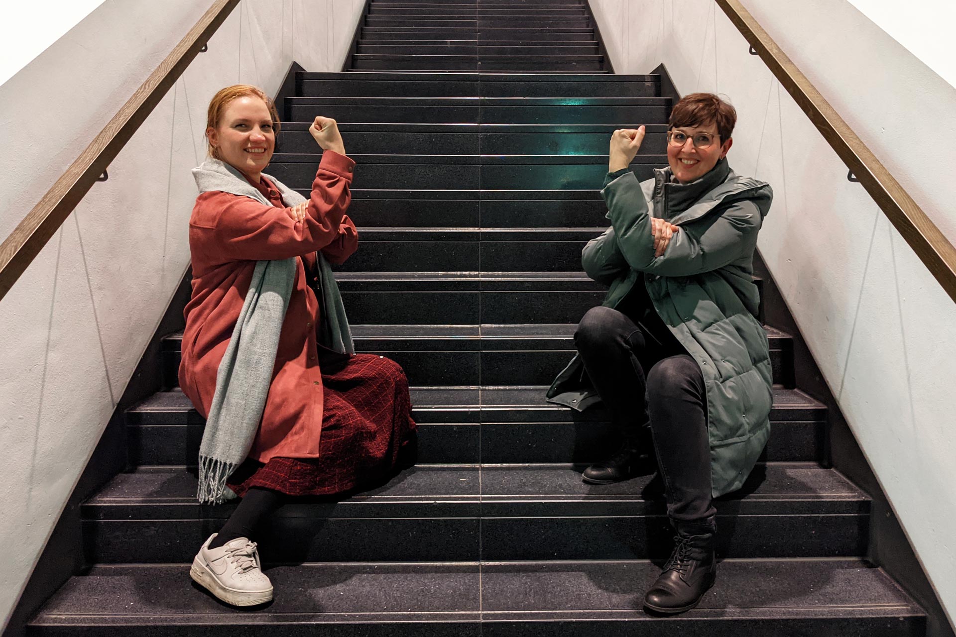 Elisa Senz und Sandra Cartes sitzen auf Treppenstufen und ballen ihre Hand zur Faust.
