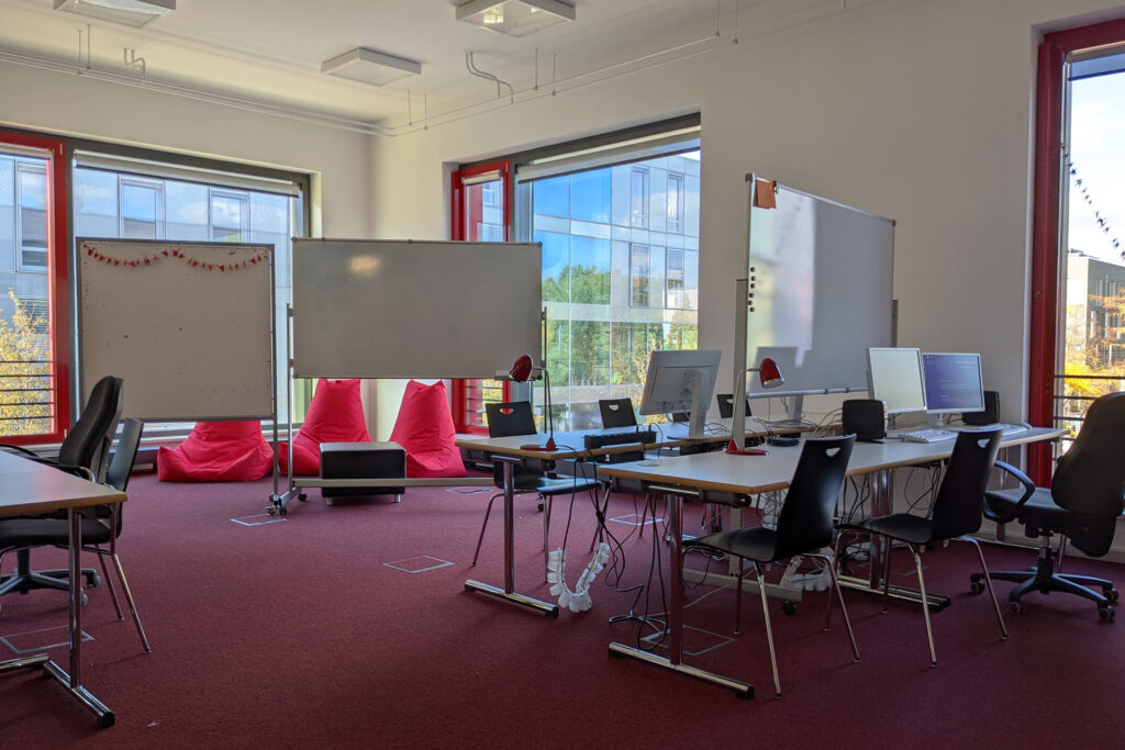 Co-Working-Space der Bibliothek: ein hell beleuchteter Raum mit mehreren Tischen, Stühlen, Whiteboards und roten Sitzsäcken.