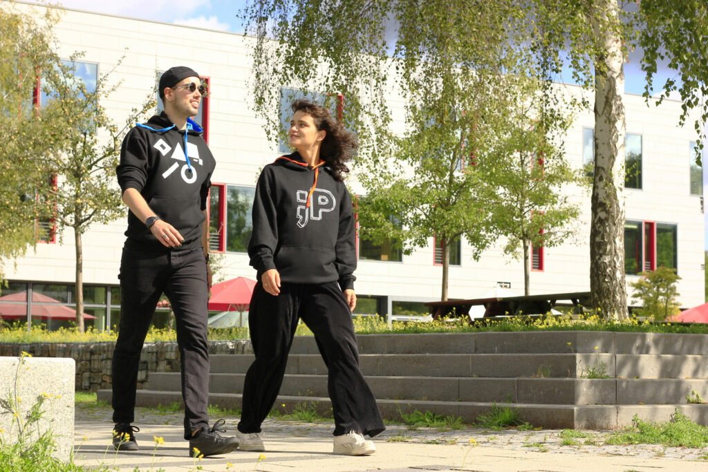 Zwei Personen laufen durch den Campus und tragen schwarze Hoodies des FHP-Merchandise.